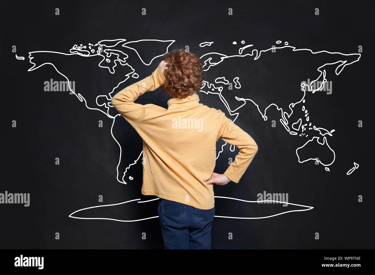 Child boy student looking at map of Earth on chalkboard background and learning geography Stock Photo