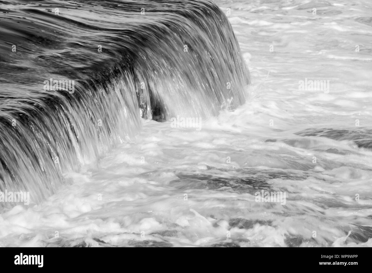 Black and White Abstract photographs of a seascape with strong backwash with water flowing over a tidal pool wall at a low shutter speed - powerful Stock Photo