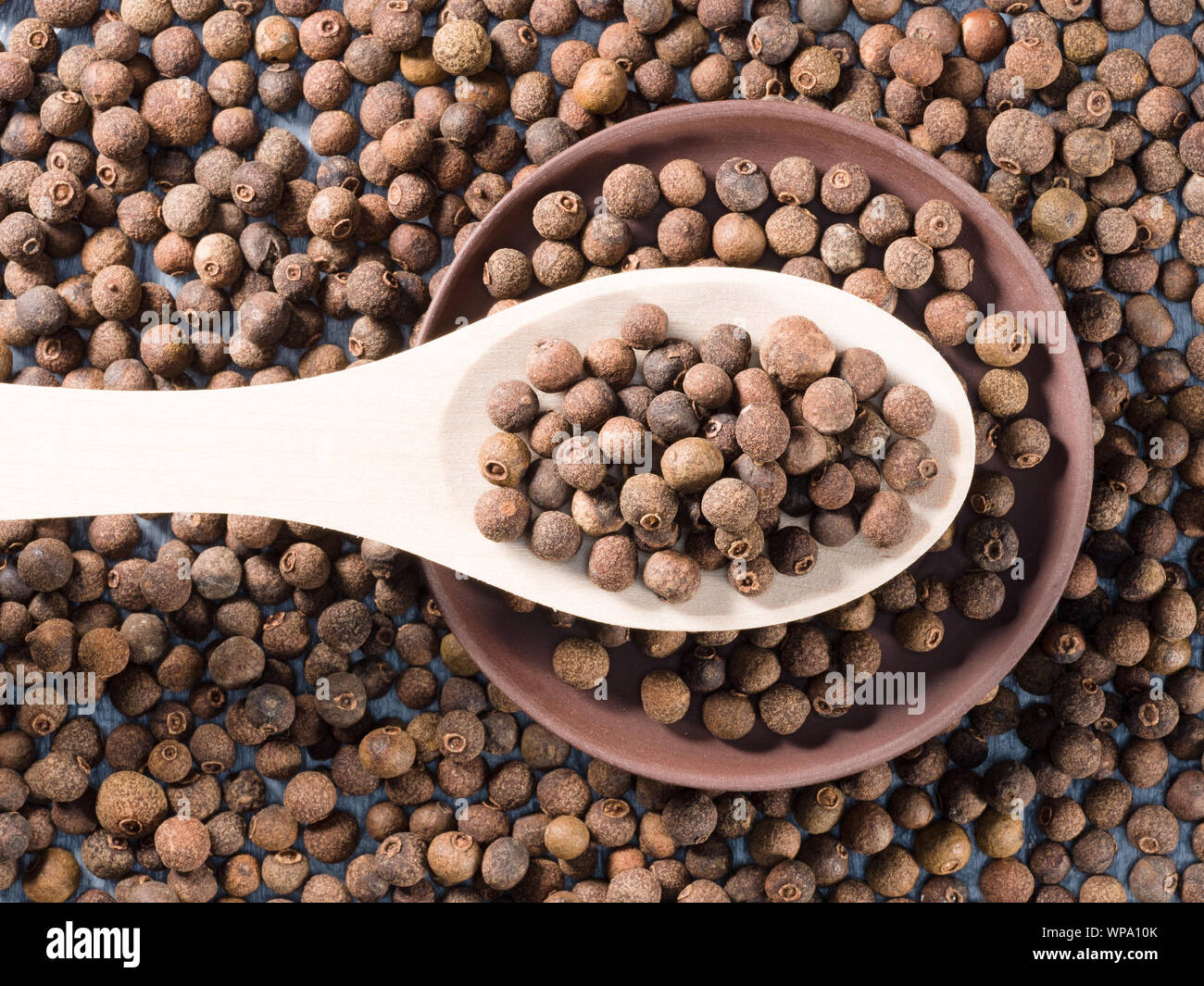 Allspice (Jamaica pepper) in a wooden spoon and clay plate on allspice