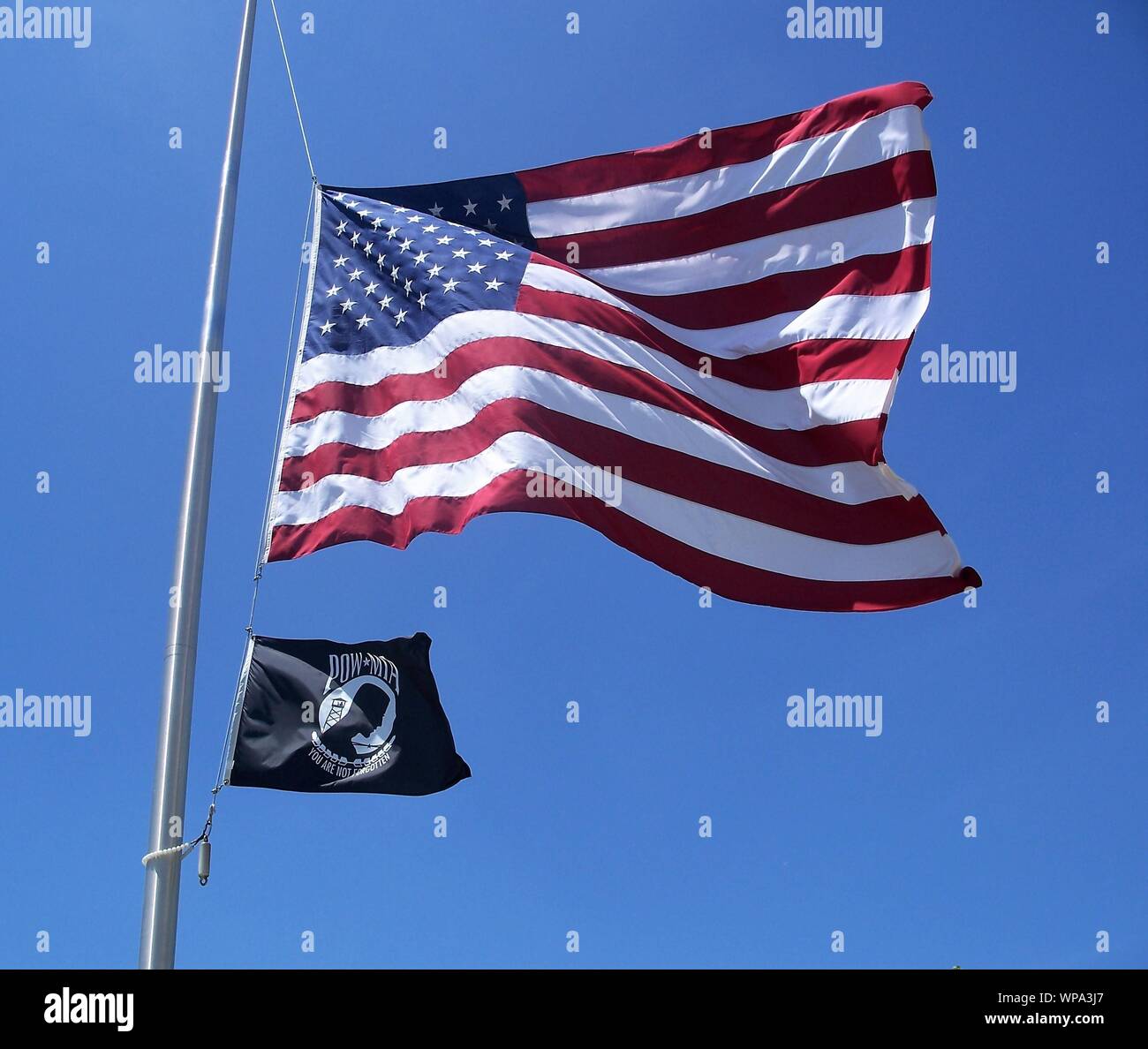 United States of America and Prisoner of War flags on a flagpole with a clear blue sky background Stock Photo