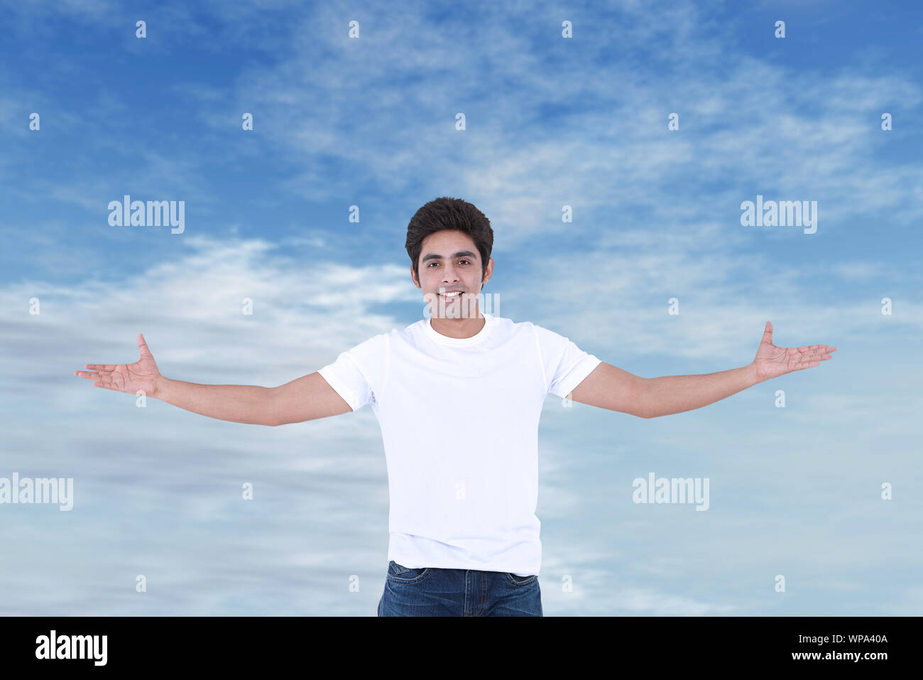 Young man standing with his arm outstretched against cloudy sky Stock Photo