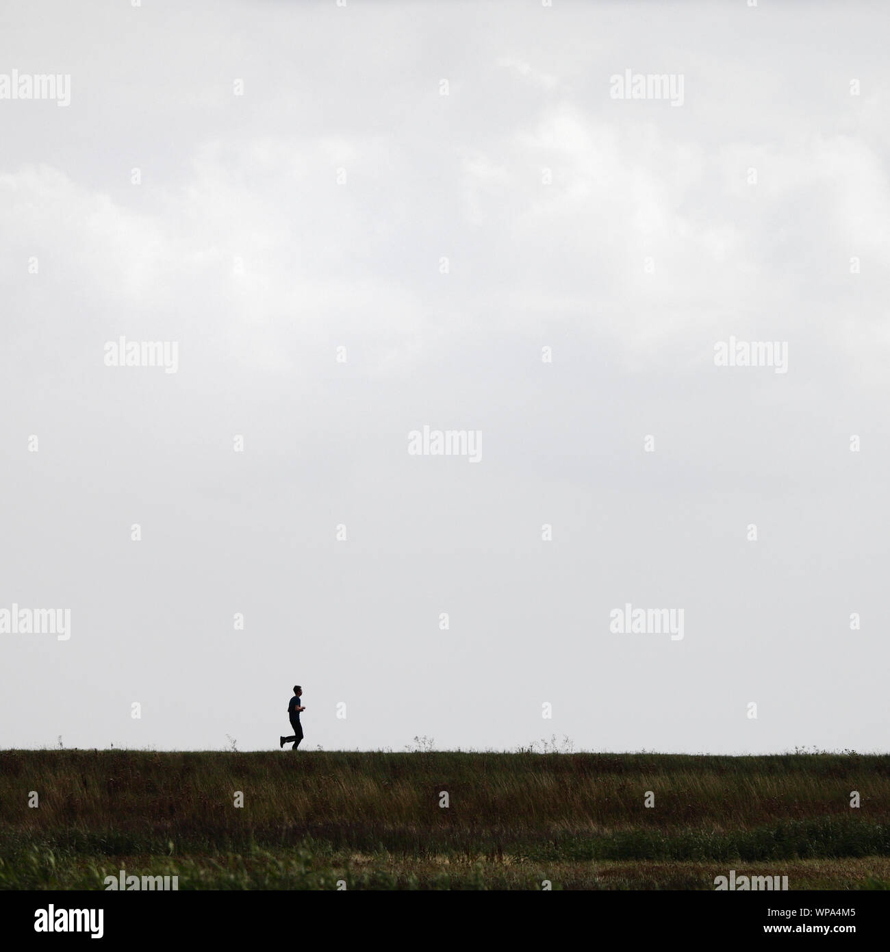 Young man running on the top of a bank in the marshes of North Norfolk. Stock Photo