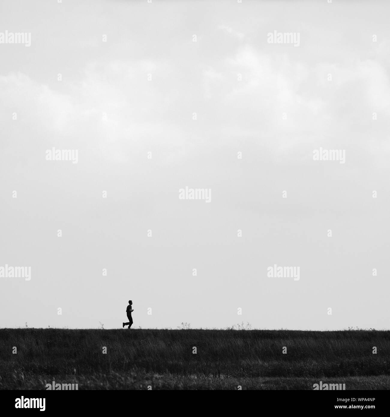 Young man running on the top of a bank in the marshes of North Norfolk. Stock Photo