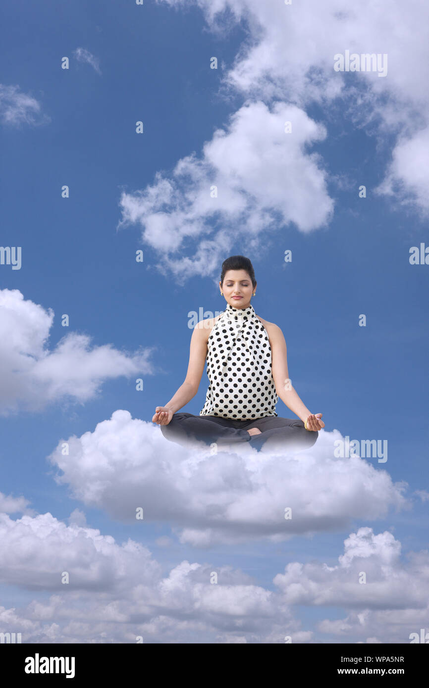 Businesswoman sitting on clouds practicing yoga Stock Photo