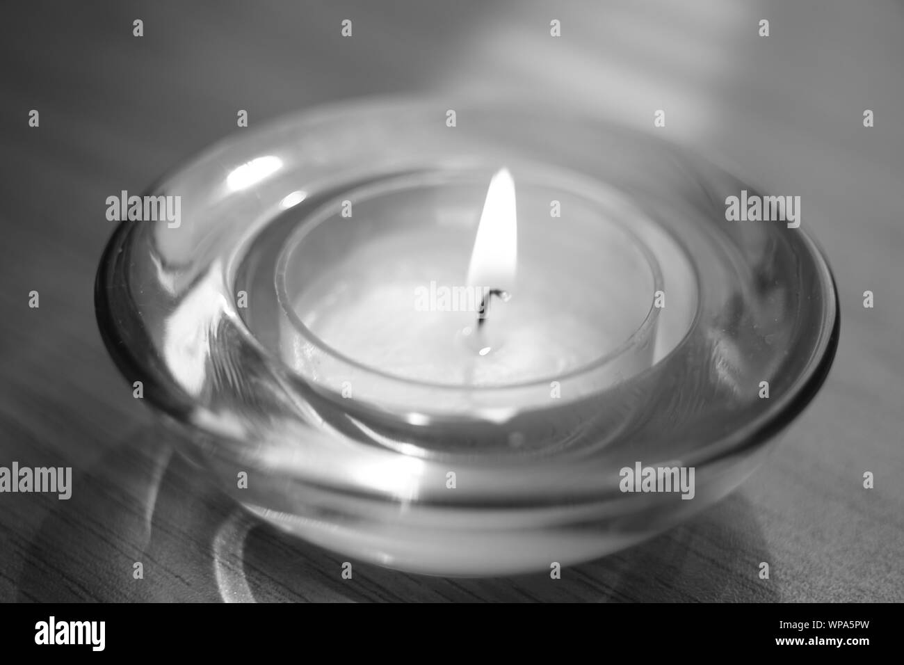 low candle burns in a round glass candlestick, closeup, bw Stock Photo