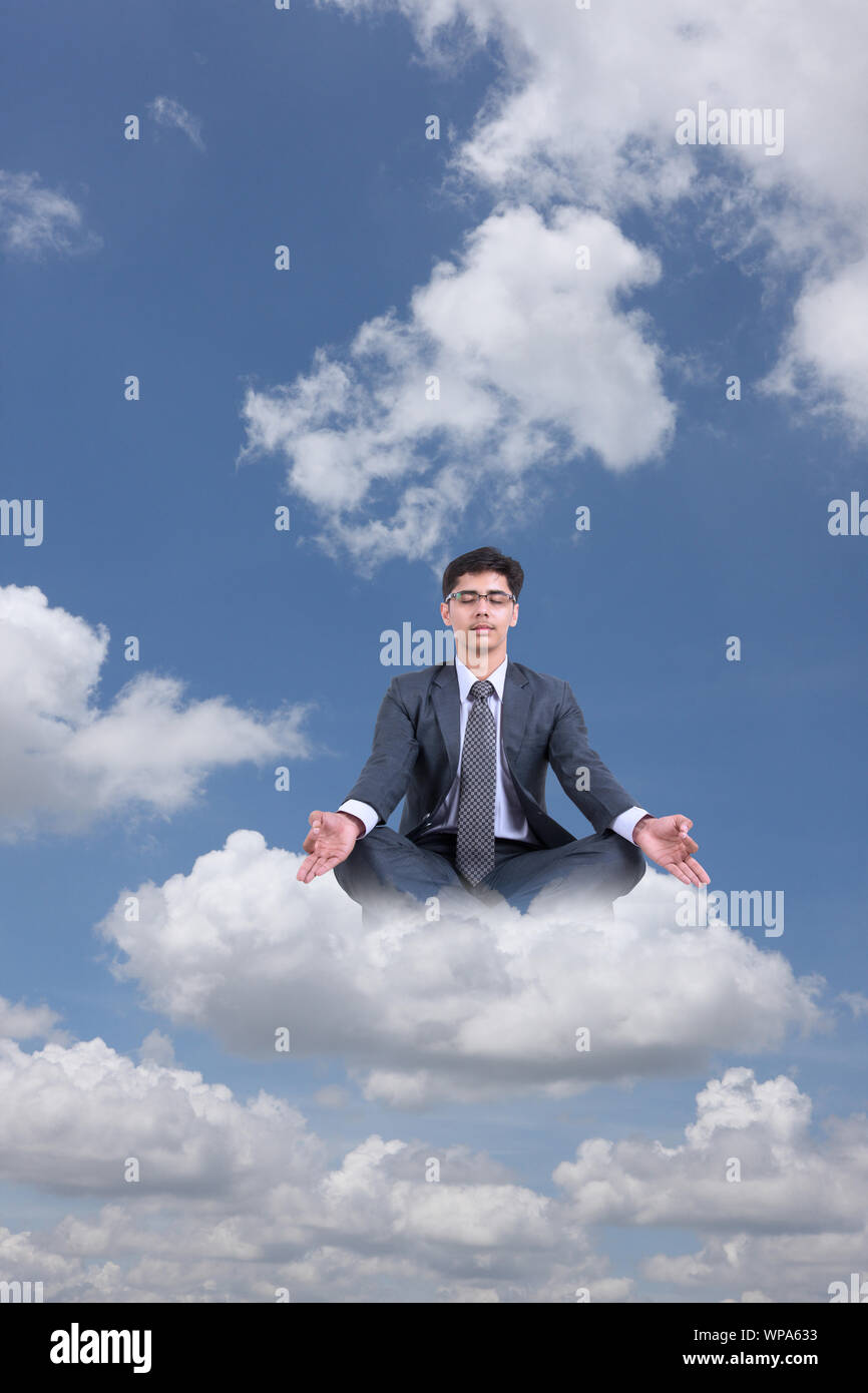 Businessman sitting on clouds practicing yoga Stock Photo