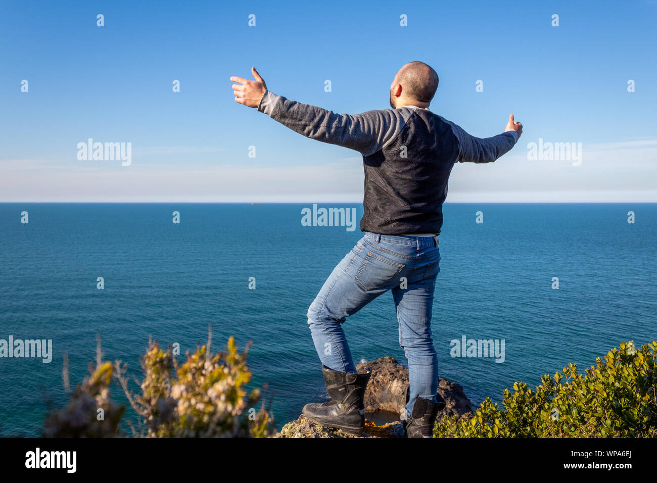 Man on the cliff with arms open against the sea and sky Stock Photo