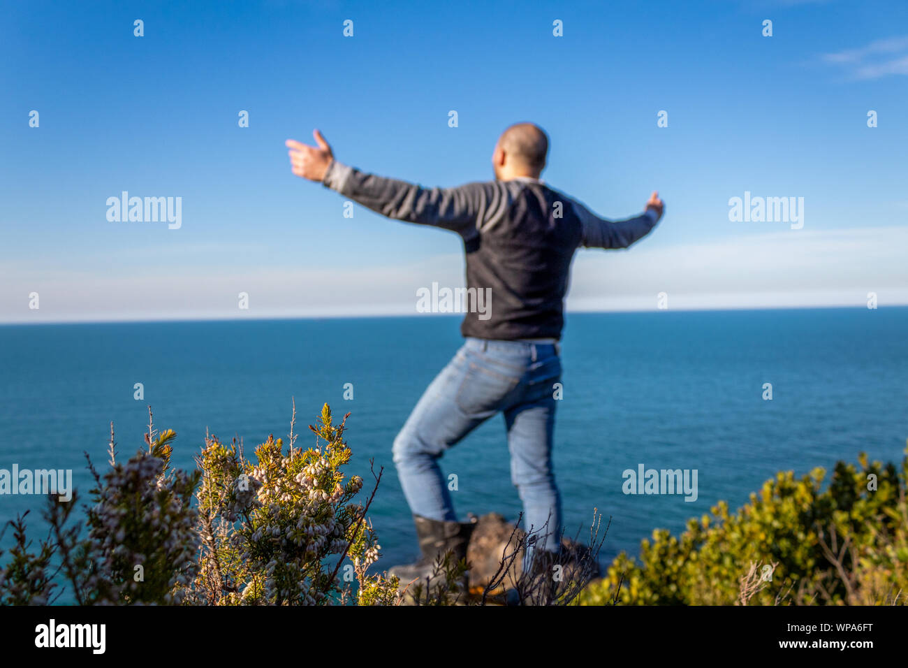 Man on the cliff with arms open against the sea and sky Stock Photo