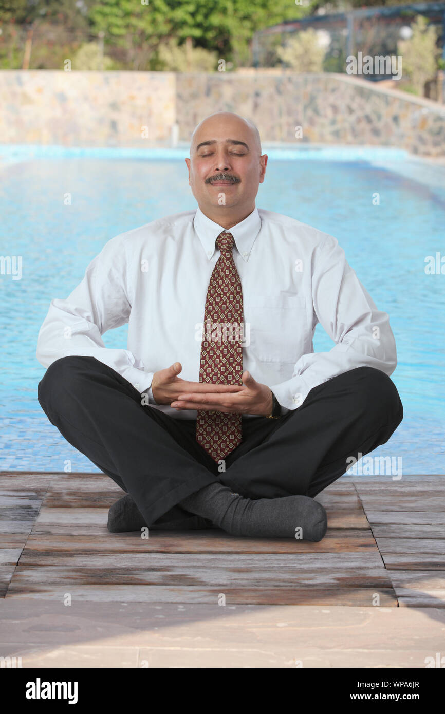 Businessman practicing yoga at poolside Stock Photo