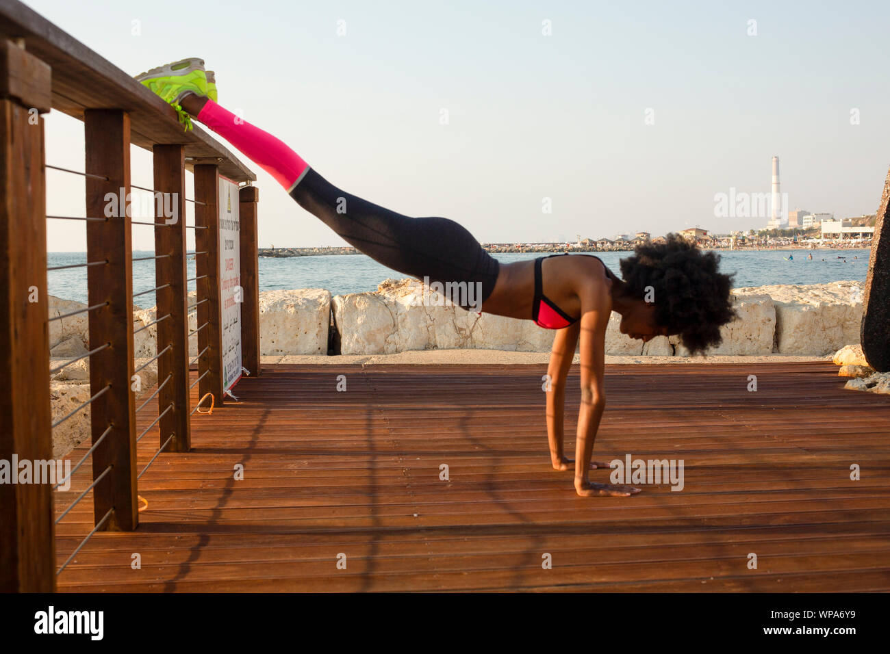 happy young african woman stretching and warming up before an outdoor workout. The Mediterranean sea in the background Stock Photo