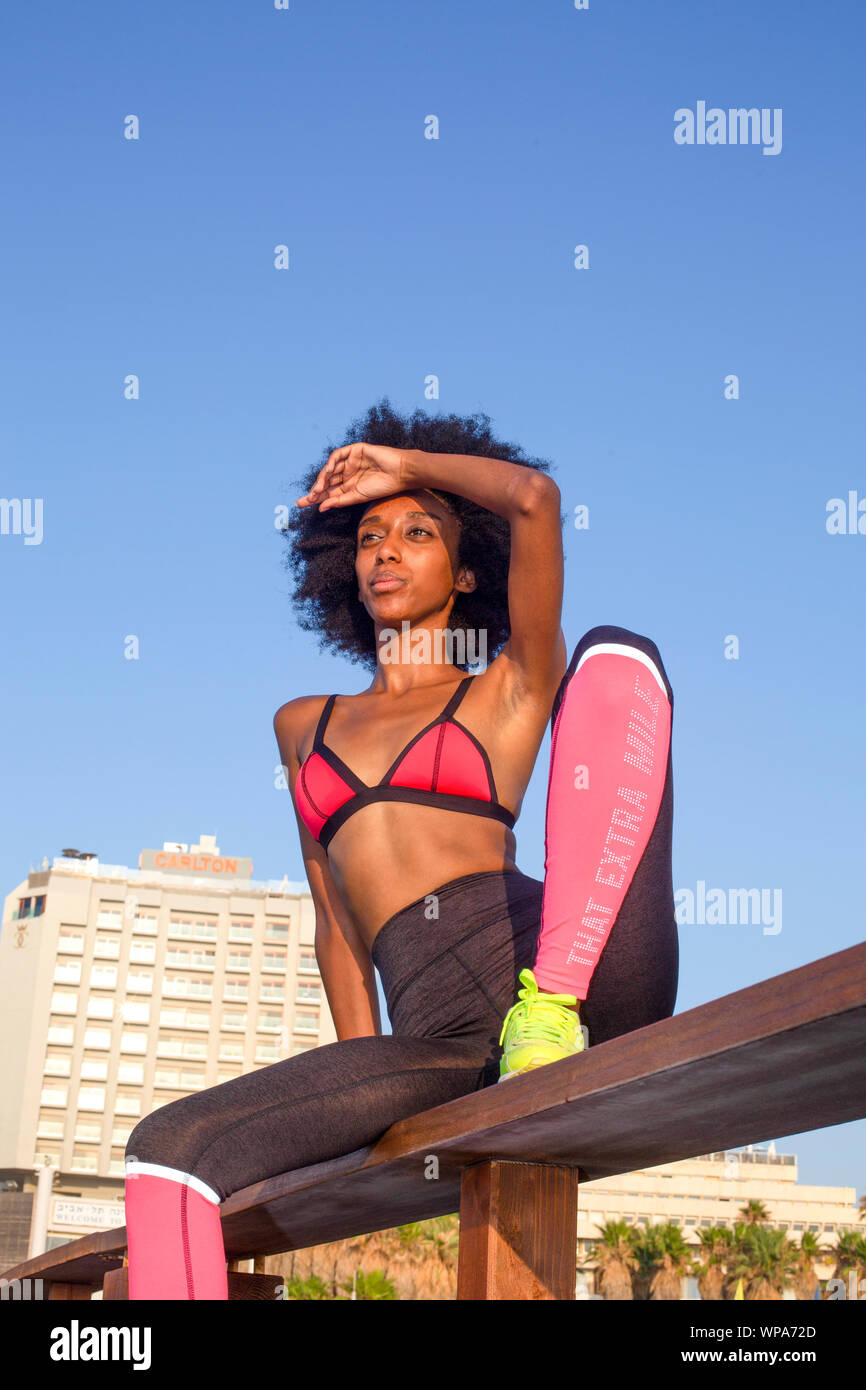 happy young african woman stretching and warming up before an outdoor workout. with a beautiful blue sky background Stock Photo