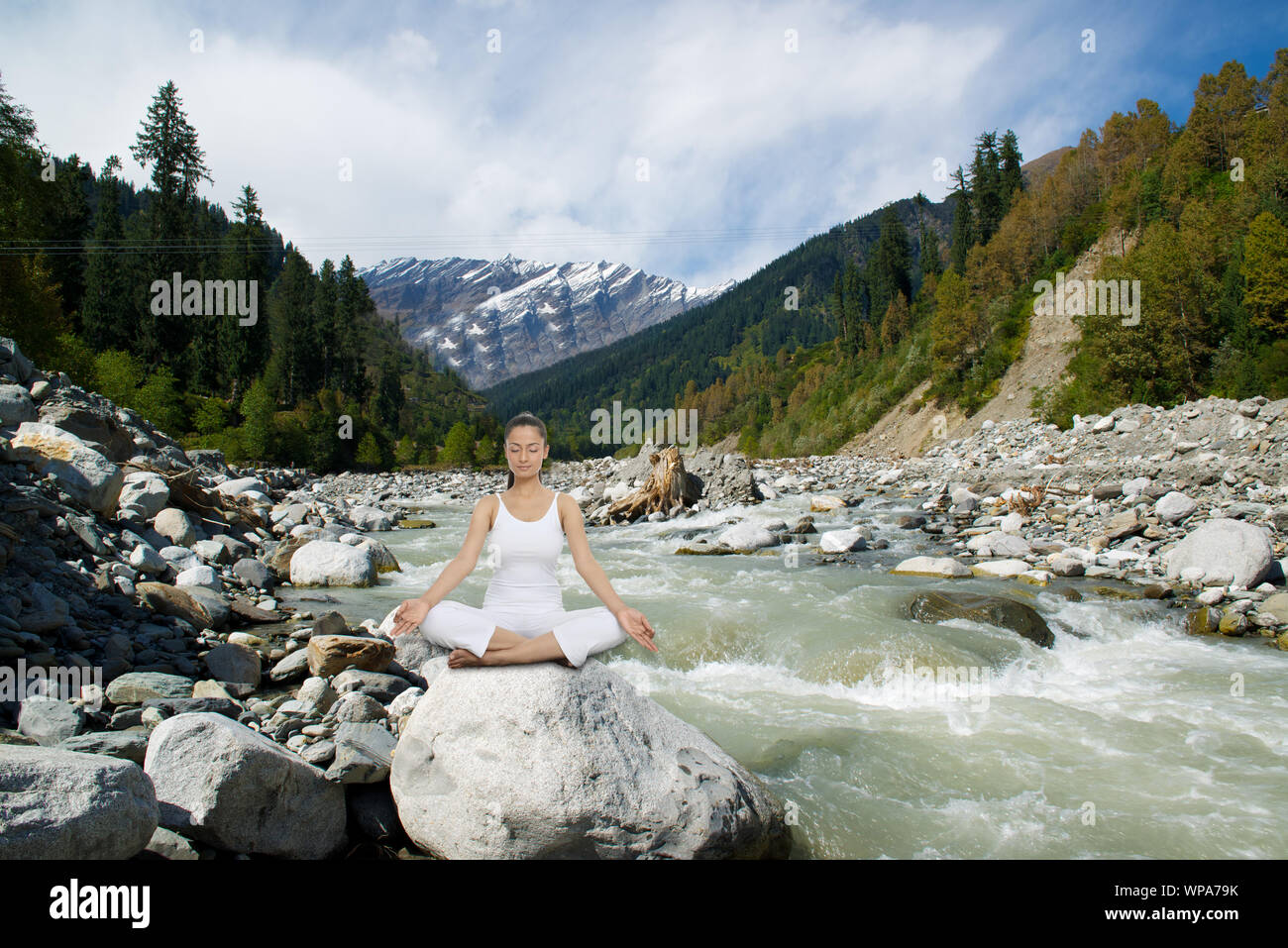Young woman practicing yoga sitting on a rock at riverbank, Beas River, Manali, Himachal Pradesh, India Stock Photo