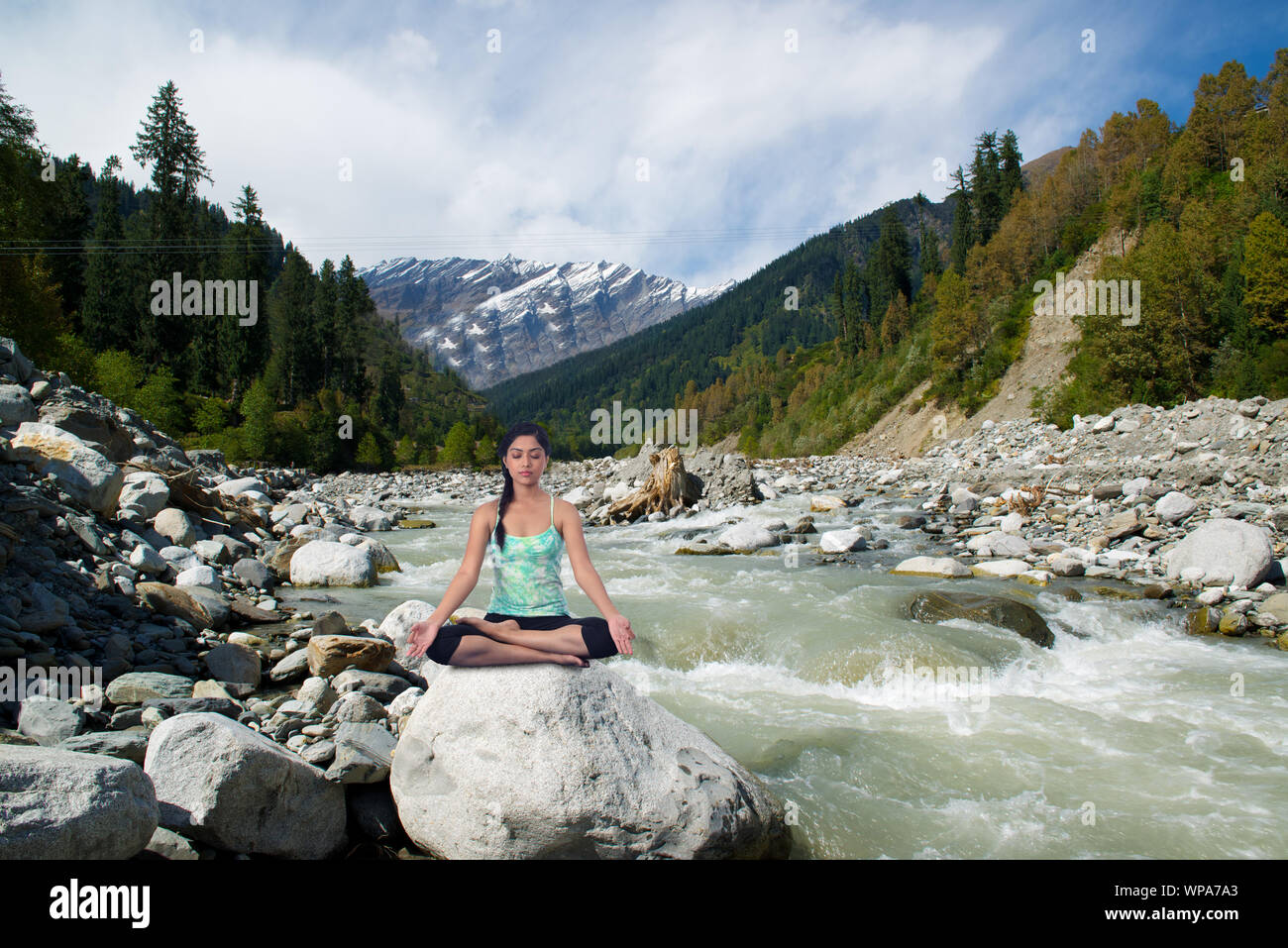 Young woman practicing yoga sitting on a rock at riverbank, Beas River, Manali, Himachal Pradesh, India Stock Photo