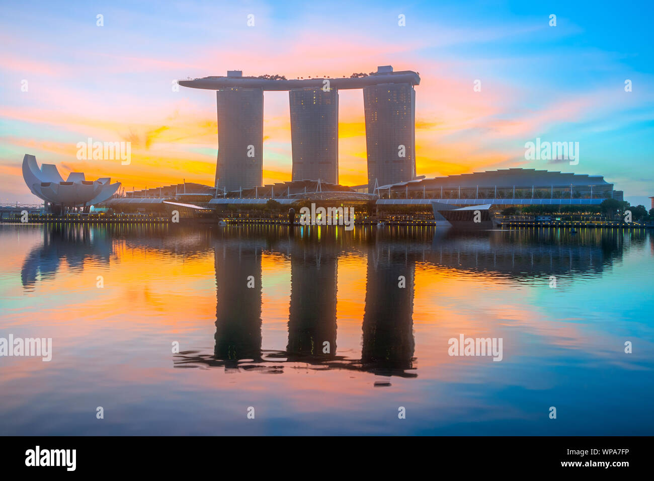 Morning in Singapore. Three buildings of the hotel in the form of a ship are reflected in the calm water of Marina Bay. The rising sun painted the sky Stock Photo