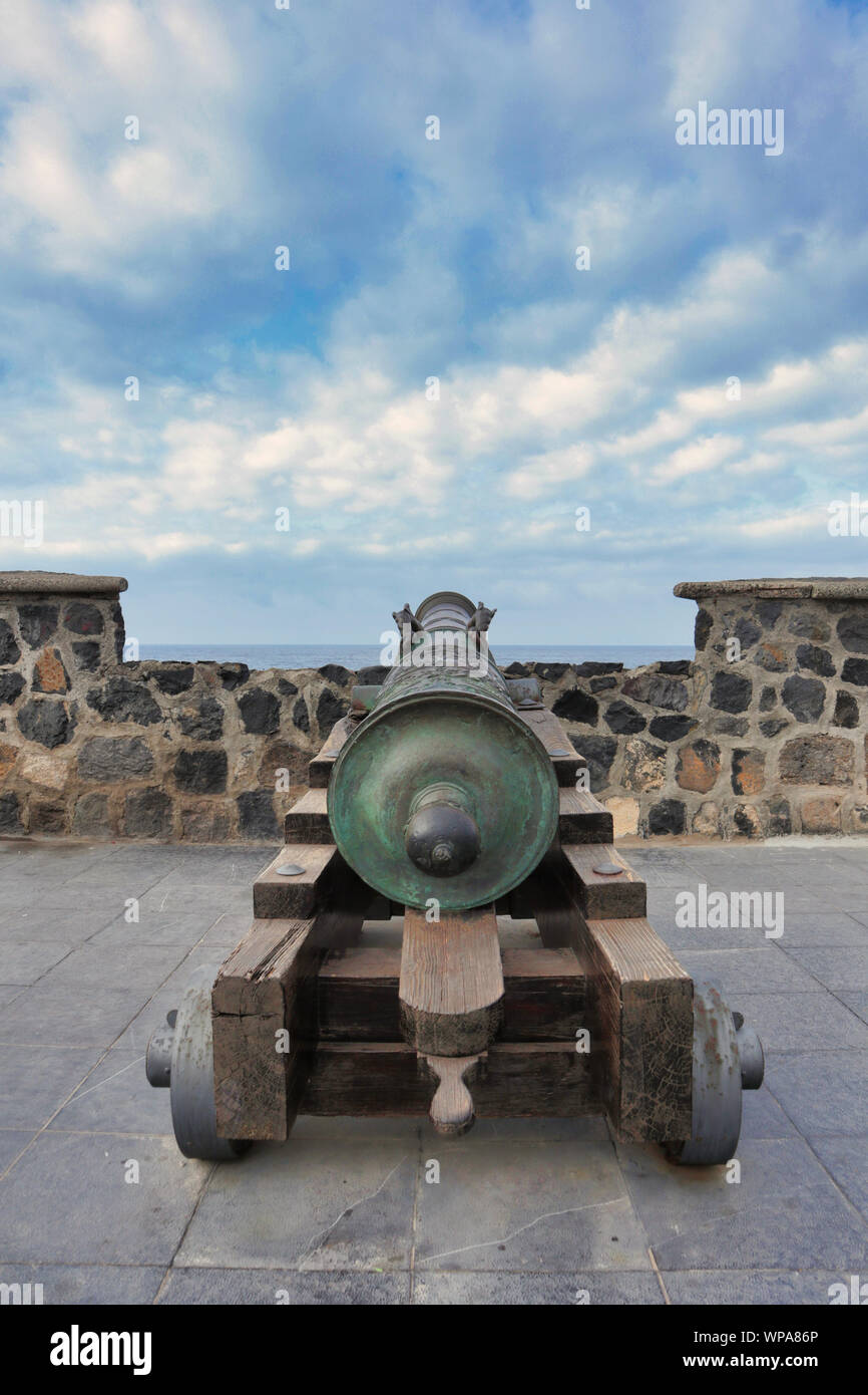 old bronze spanish naval cannon on a wooden carriage on a wall of fortress in port of Puerto de la Cruz facing open sea, Tenerife, Canary Islands Stock Photo