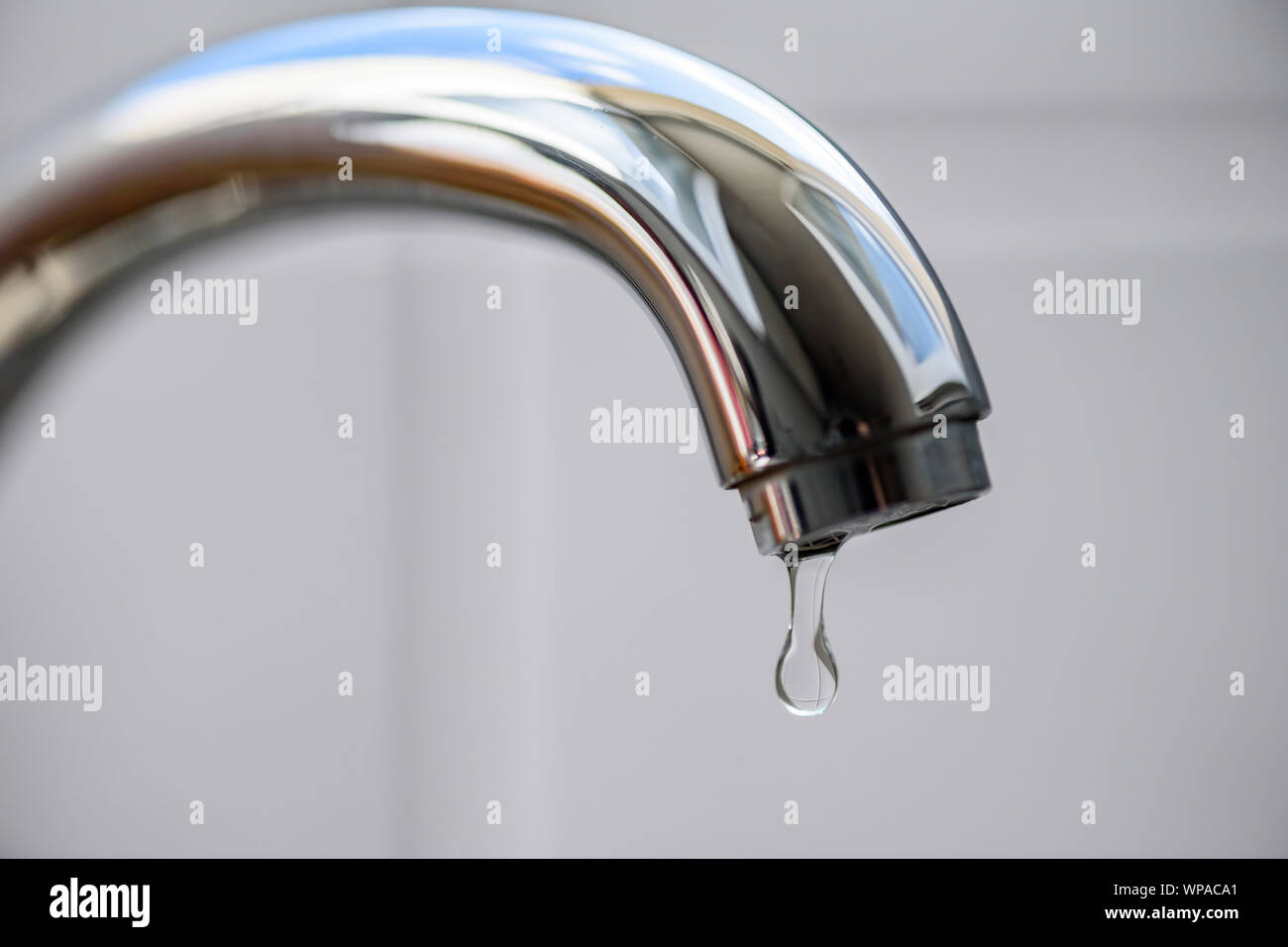 Clean water drop falling from a dripping kitchen faucet, an unnecessary waste of water in a world threatened by water scarcity. Stock Photo