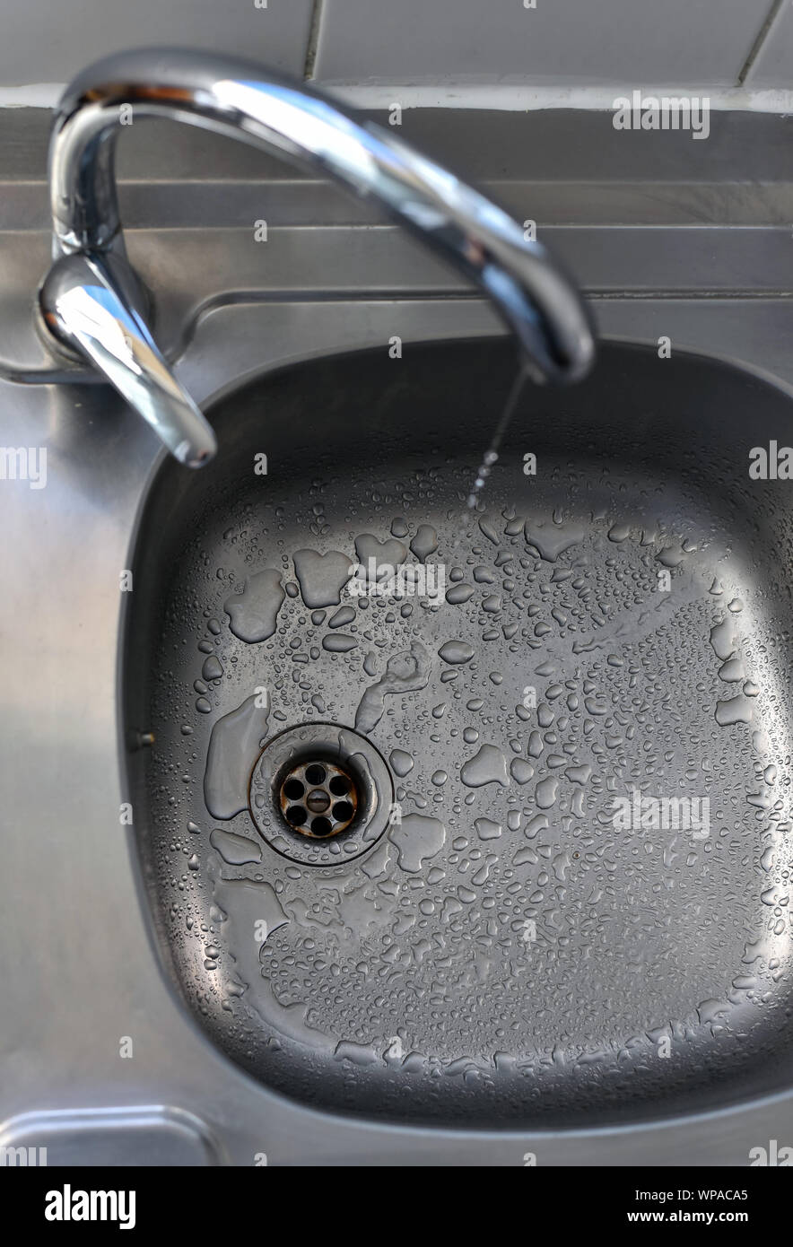 Clean water drops falling from a dripping kitchen faucet, an unnecessary waste of water in a world threatened by water scarcity. Stock Photo