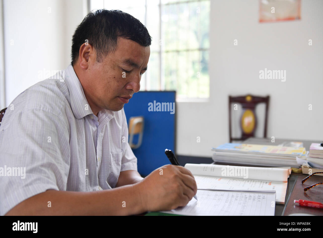 (190908) -- TIANDONG, Sept. 8, 2019 (Xinhua) -- Wei Guoji prepares lessons at the office of Tuogua Primary School at Tuogua Village in Zuodeng Yao Ethnic Township of Tiandong County, south China's Guangxi Zhuang Autonomous Region, Sept. 3, 2019. Located in remote mountains of Tiandong county, Tuogua primary school is over 60 km away from the county seat, to which only a rugged mountain road can lead.     The 53-year-old Wei Guoji, a native to the village, is the principal of the village school. Wei was recruited as a substitute teacher of the school after graduation from junior high school at Stock Photo