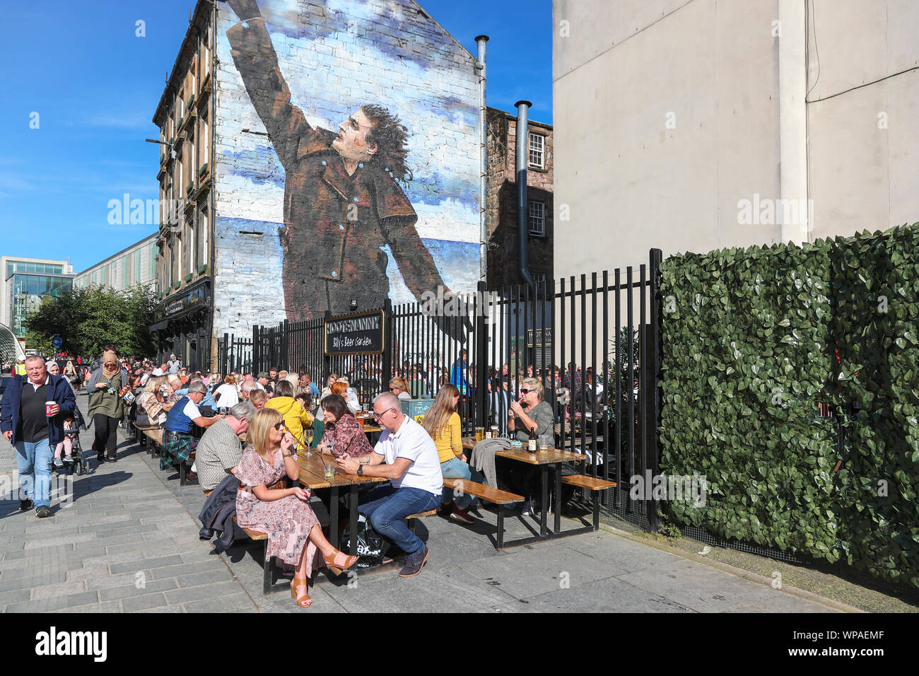 Tourists sitting on the outdoor seating at the Hootenanny pub in the area named Billy' Beer garden after the wall mural of Billy Connolly, the famous Stock Photo