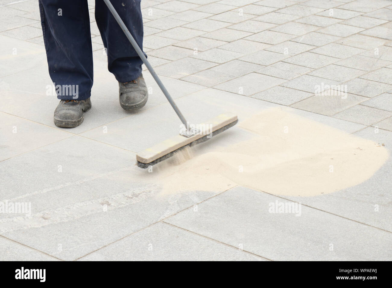 Pavement construction worker filling the block joints with sand using long broom, finishing road paving Stock Photo