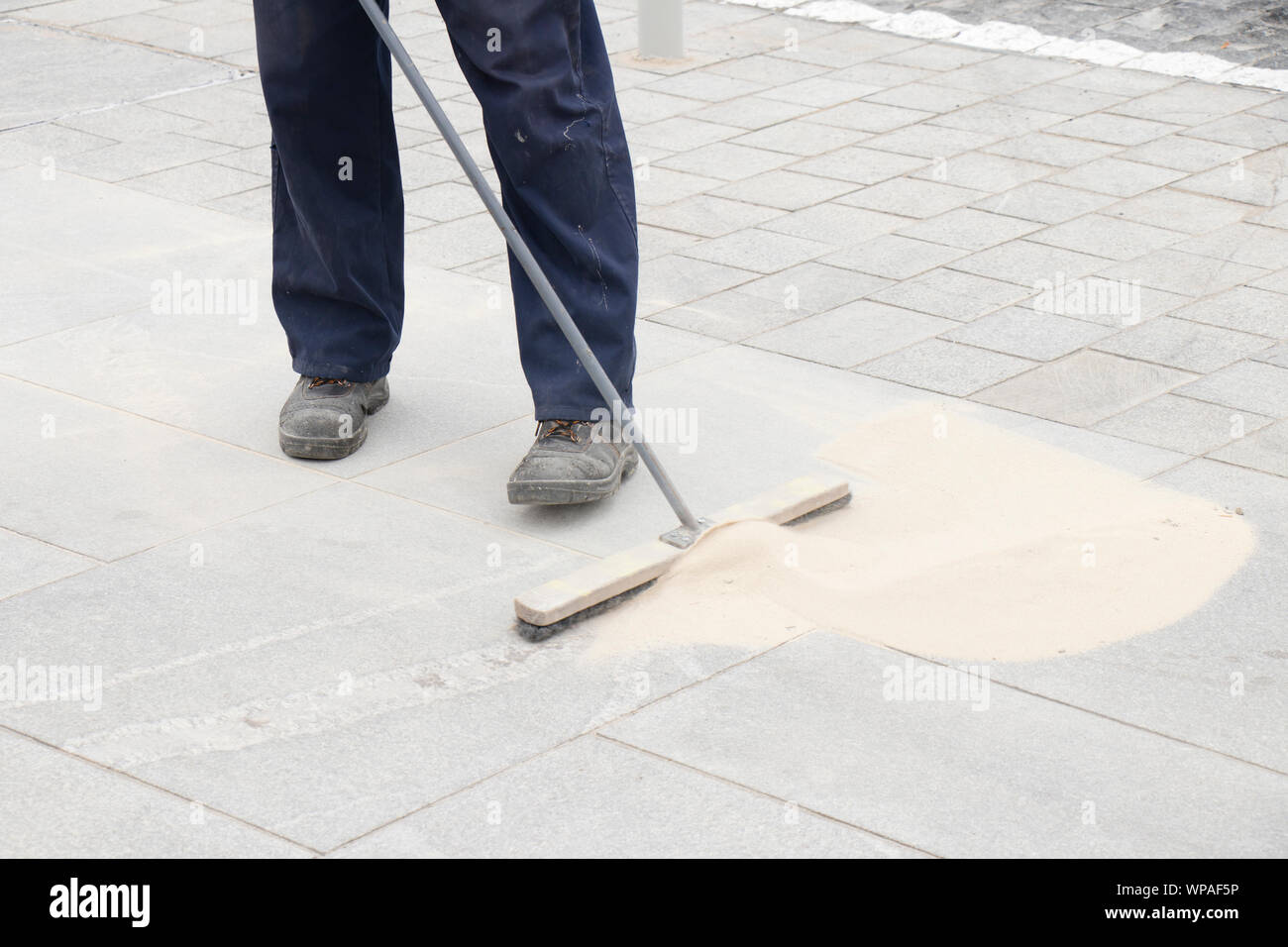 Pavement construction worker filling the block joints with sand using long broom, finishing road paving Stock Photo