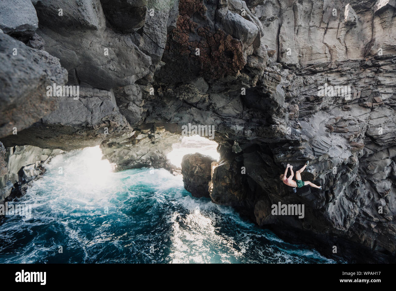 Man climbing above the ocean in a volcanic cave Stock Photo
