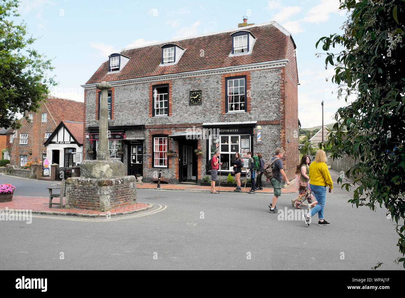Shops, people tourists with rucksacks walking outside and view of the main high street in Alfriston Village in East Sussex, England, UK  KATHY DEWITT Stock Photo