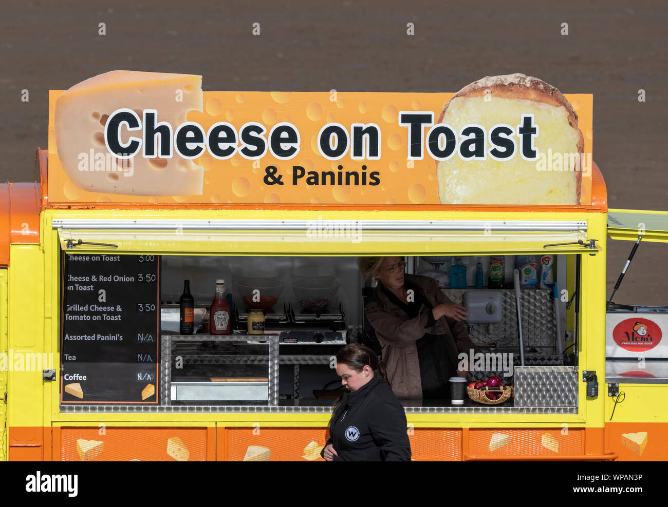 Young woman walking past a mobile food concession selling Cheese on Toast. Southport Beach, Merseyside, UK Stock Photo