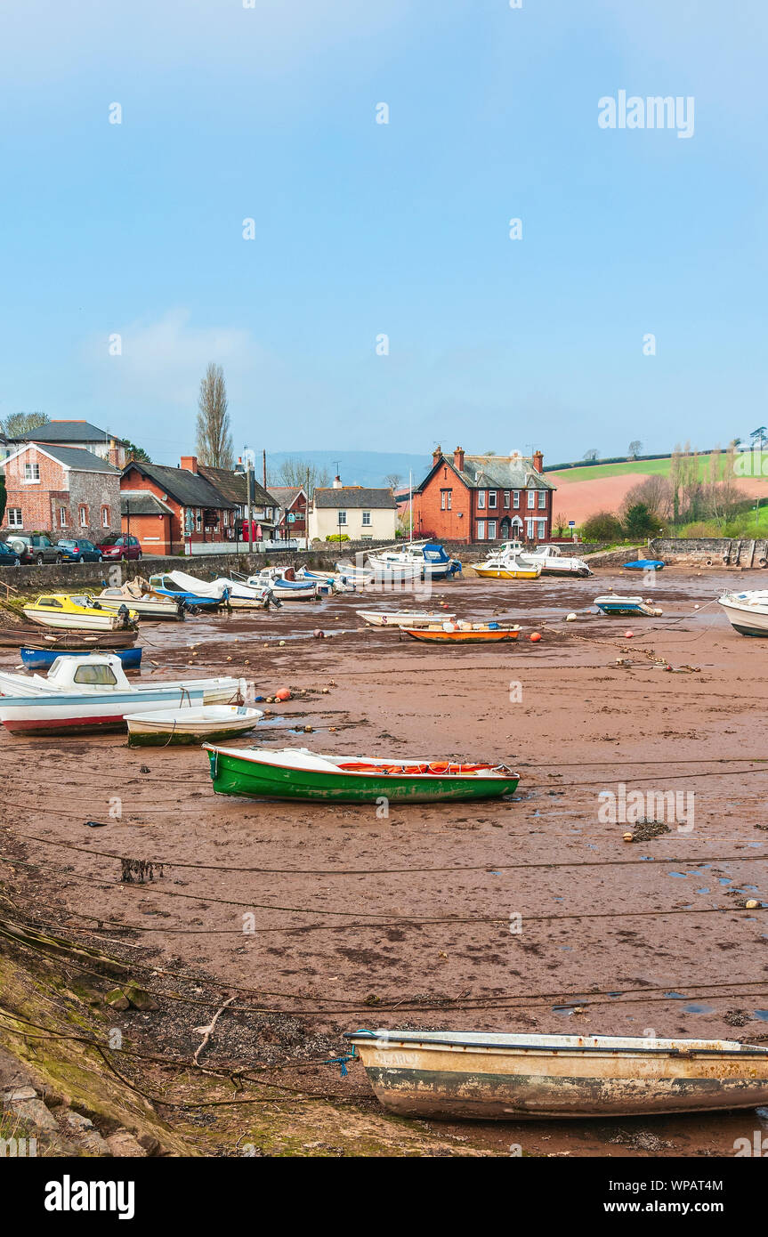 Mist partially obscures a large hill behind a picturesque village road alongside the boats moored on exposed mudflats of Cockwood tidal harbour Stock Photo