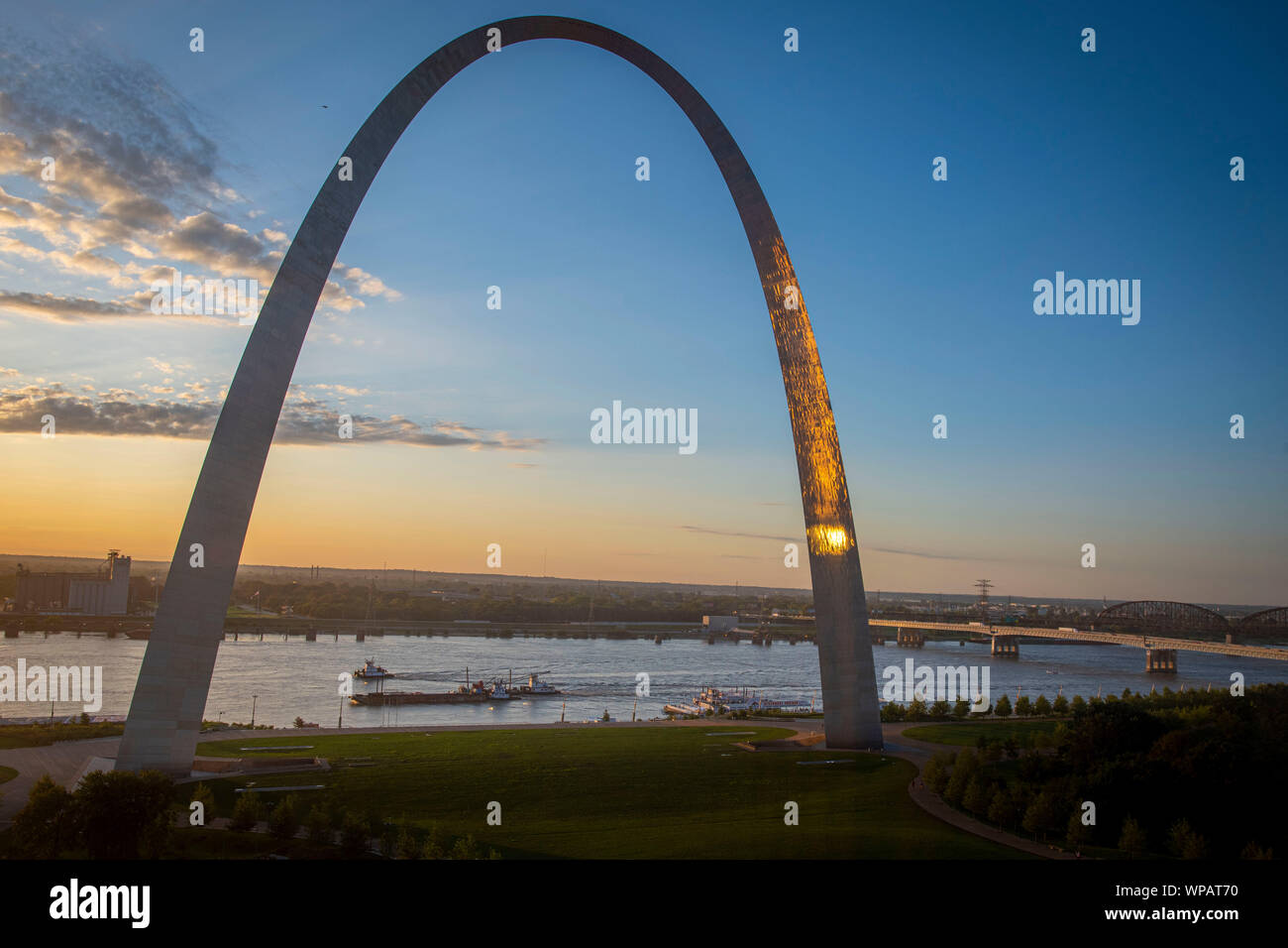 Barge traffic on the Mississippi River pass the Gateway Arch National Monument at sunset August 29, 2019 in St. Louis, Missouri, USA. A typical barge carries 1500 tons of cargo, which is 15 times greater than a rail car and 60 times greater than one trailer truck. An average river tow on the Mississippi River is 15 barges consisting of 5 barges tied together and moving 3 abreast. The same load would require a train 3 miles long or line of trucks stretching more than 35 miles. Stock Photo