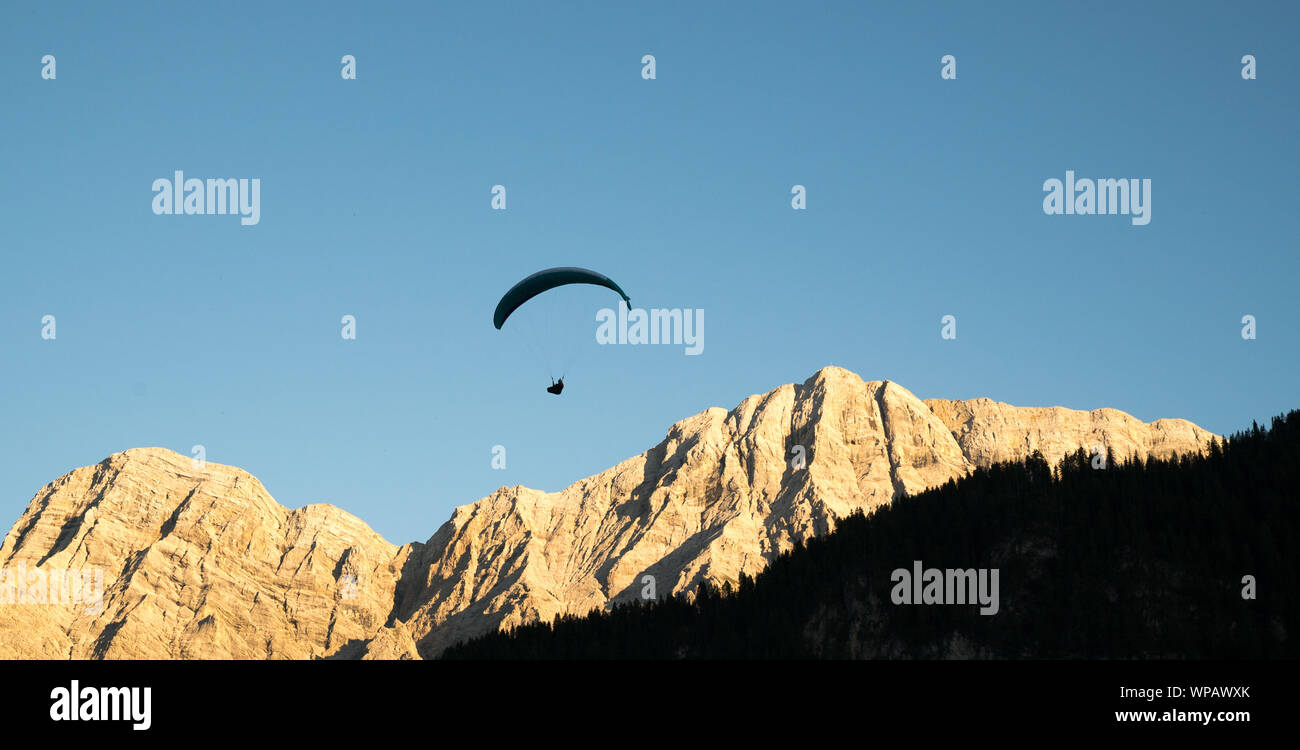 silhouette of paraglider in Dolomite mountain landscape in evening light near La Valle Stock ...