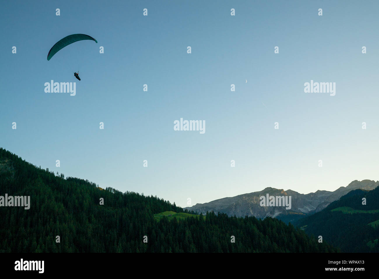 silhouette of paraglider in Dolomite mountain landscape in evening light near La Valle Stock ...