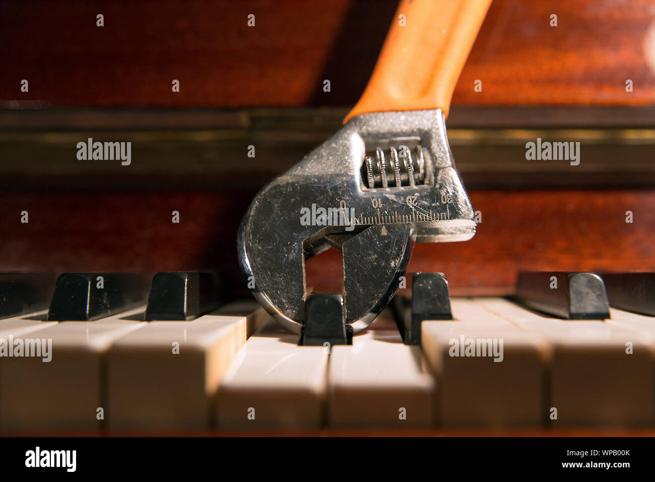 Close up of an adjustable wrench holding and pressing a piano key. Fine tuning, fat finger in financial markets, dissonance in music concepts. Stock Photo