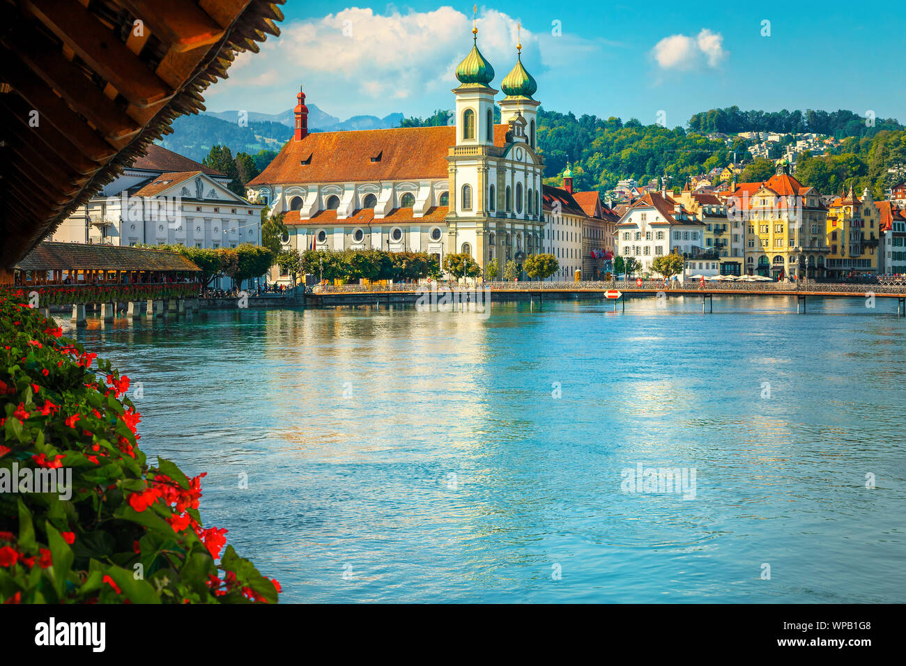 Popular touristic and travel location in Lucerne. Amazing Jesuitenkirche church with Reuss river. Spectacular view from the flowered wooden Chapel bri Stock Photo