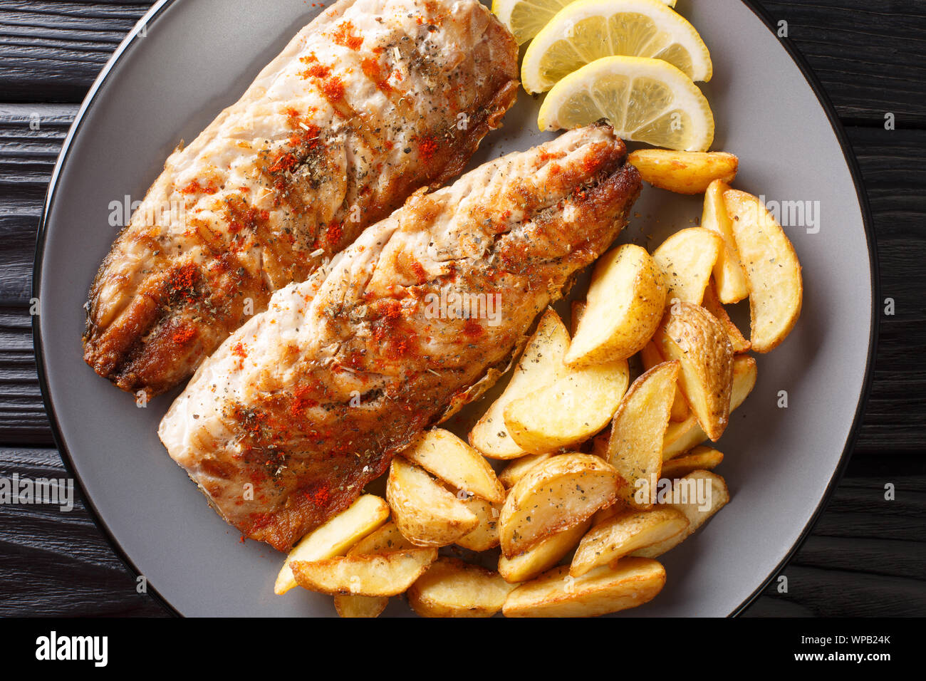Grilled mackerel served with potato wedges and lemon closeup on a plate ...