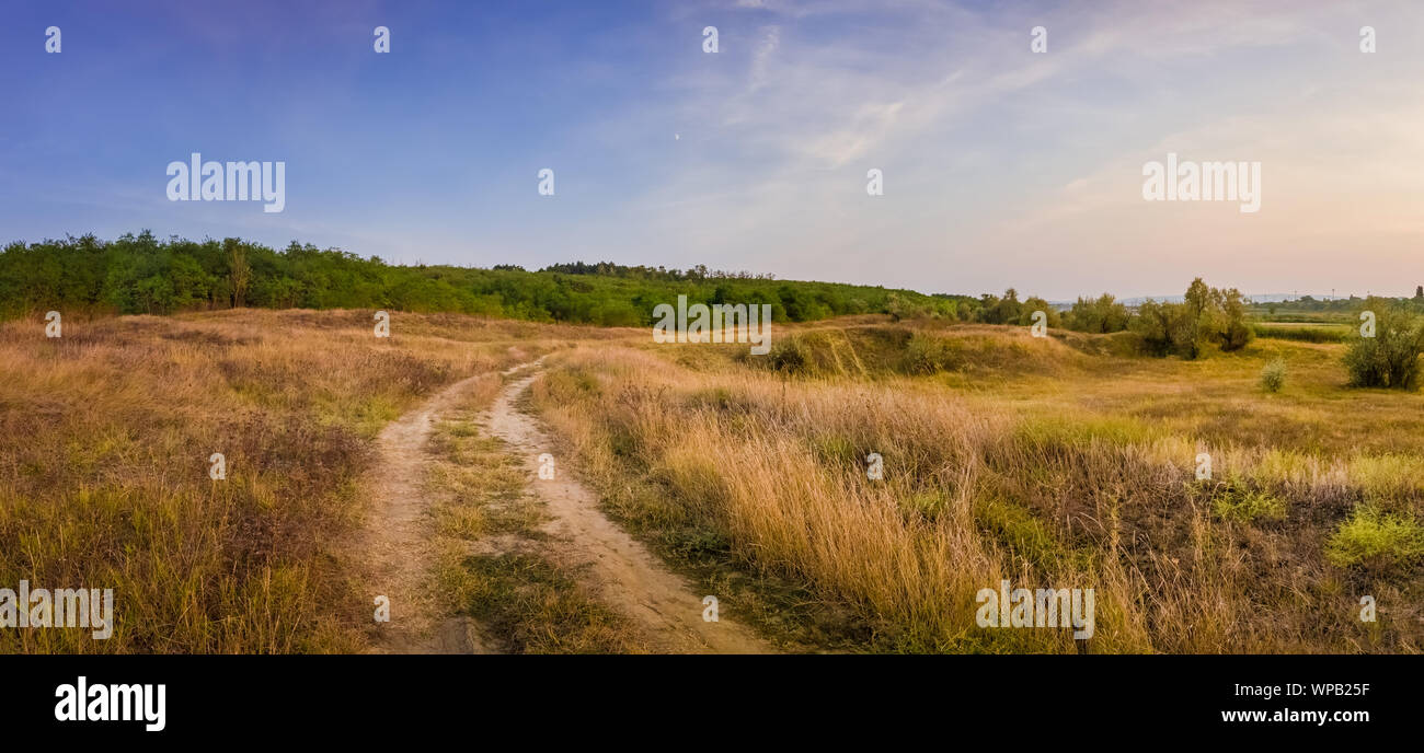 Idyllic autumn rural panorama with and a country track across a meadow with dry grass and hay. Beautiful evening scene, peaceful sunset light over the Stock Photo