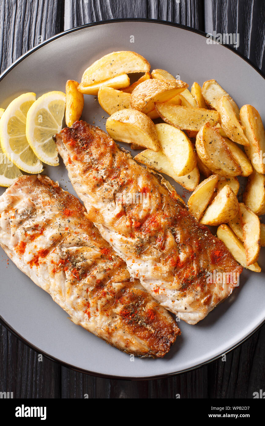 Grilled mackerel fillet with potato wedges and lemon closeup on a