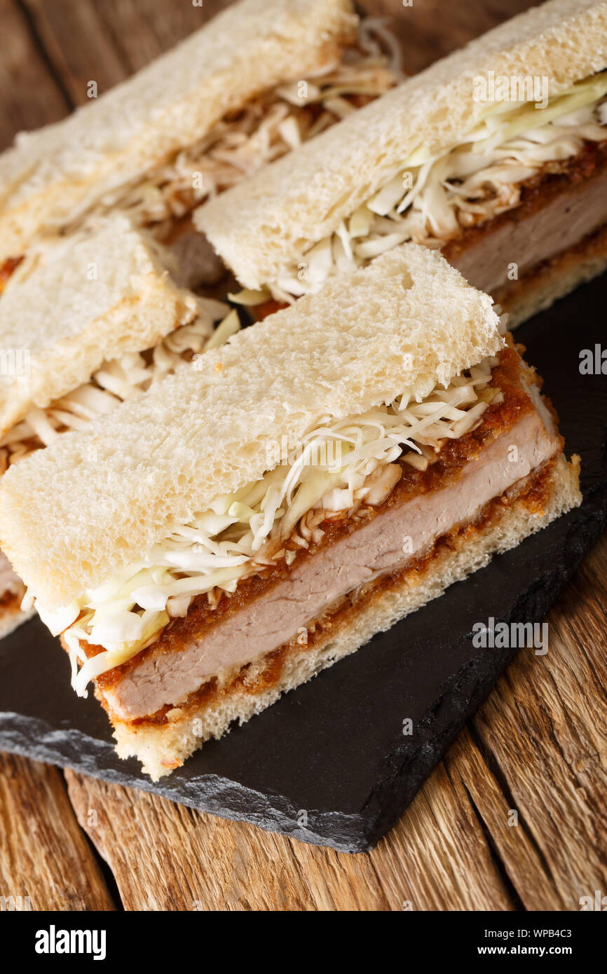 Homemade tender katsu sando sandwiches with tonkatsu sauce and cabbage close-up on a slate board on the table. vertical Stock Photo