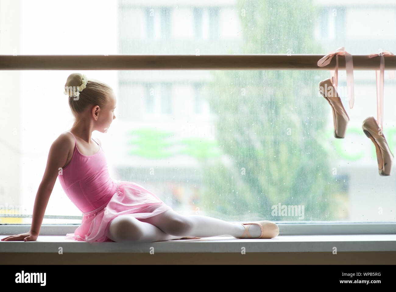 Young ballerina looking on rain outside the window. Stock Photo