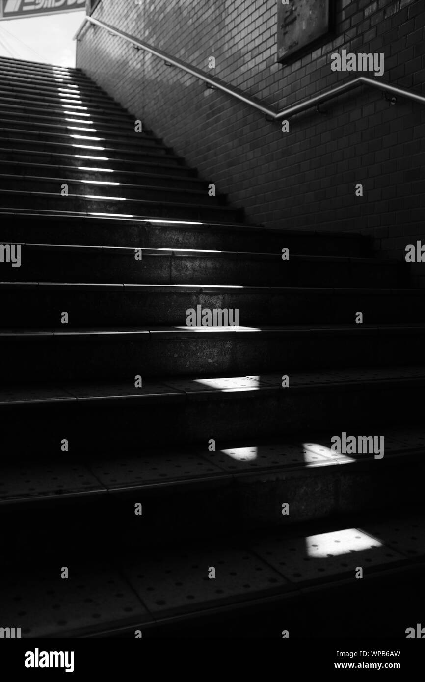 Grayscale vertical shot of stairs with a handrail on a brick wall Stock Photo