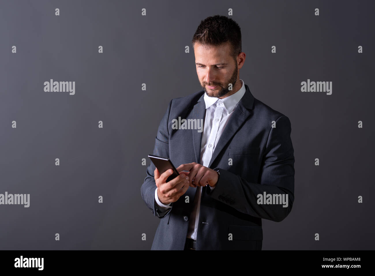 A serious handsome young businessman in a suit using his smartphone in ...