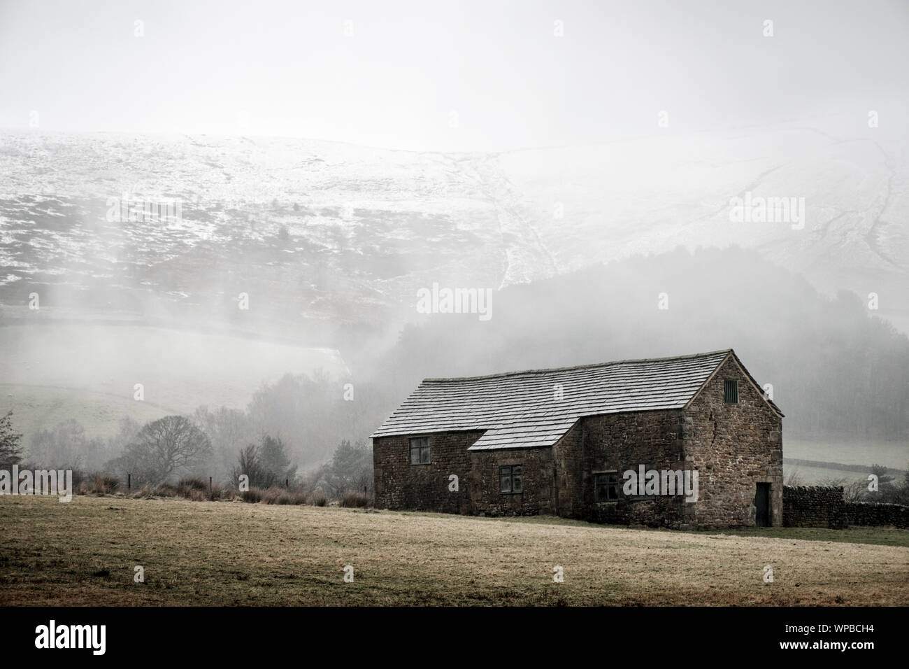 Snow storm approaching a stone barn in a countryside field in Winter with Kinder Scout in the background. Derbyshire, Peak District, England, UK Stock Photo