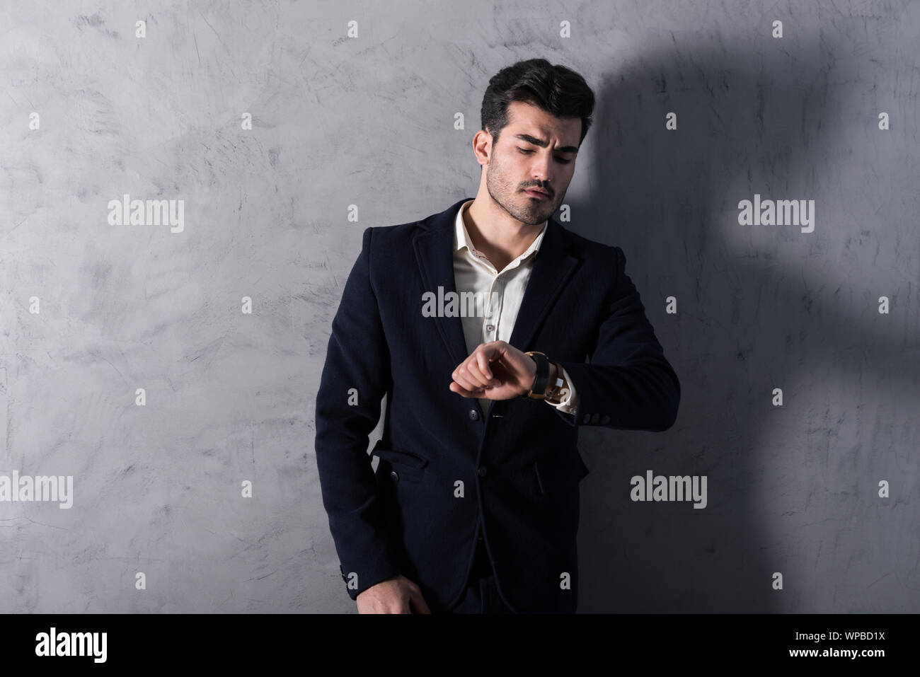 A serious handsome young businessman in a black suit checking the time ...