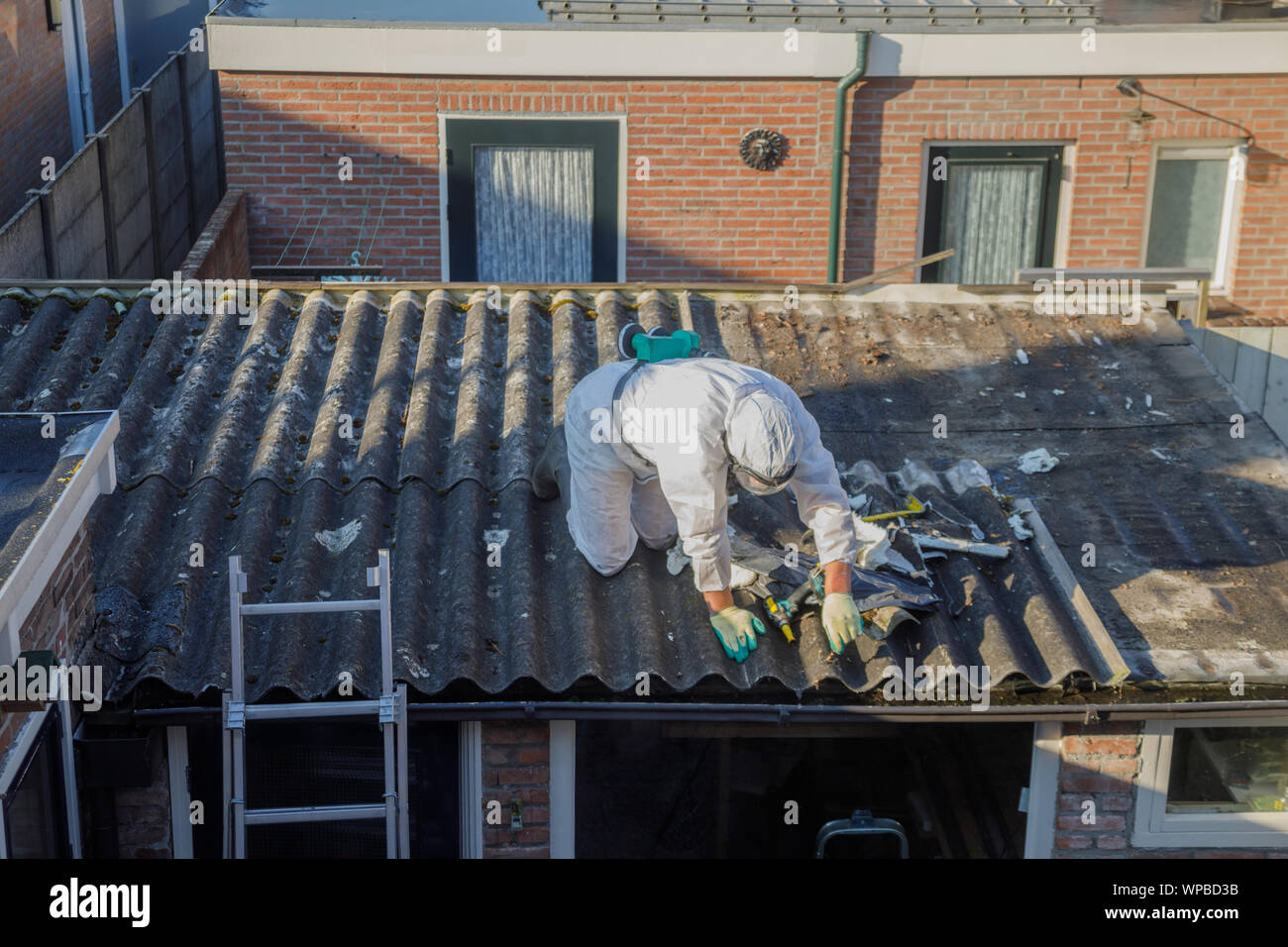 Professional asbestos removal. Men in protective suits are removing asbestos cement corrugated roofing Stock Photo