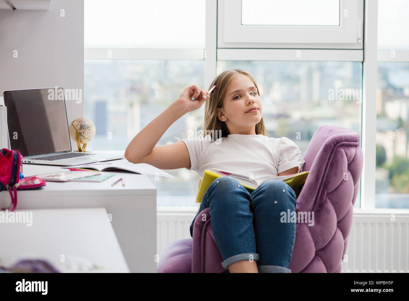 Dreaming pretty school girl with book and pencil. School supplies and laptop in background. Stock Photo
