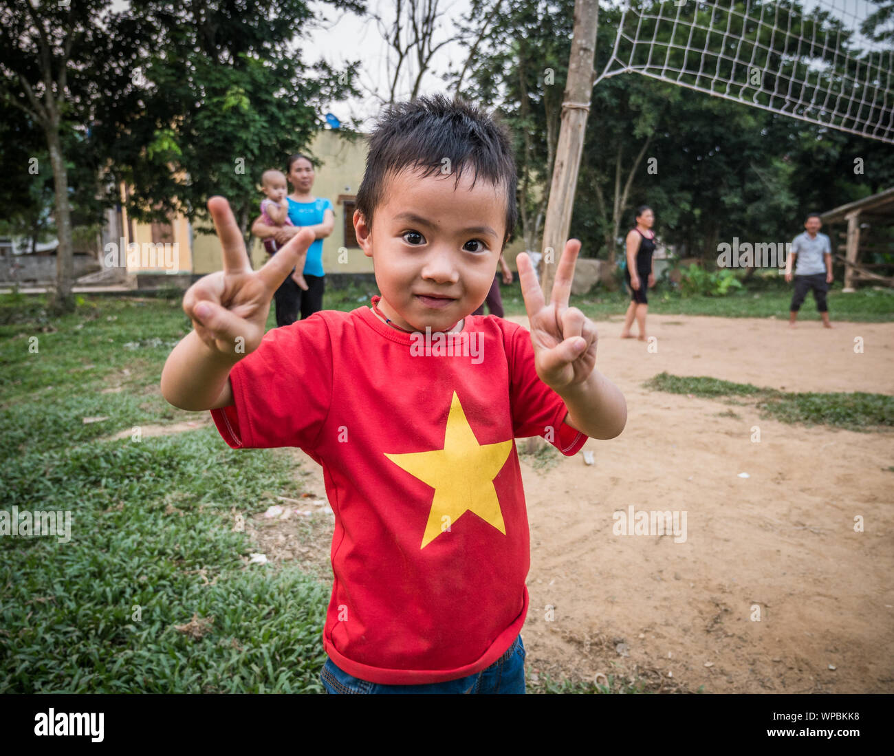 Young Vietnamese boy with Vietnam flag t-shirt showing peace symbol with both hands at a volleyball field, Phong Nha, Vietnam Stock Photo