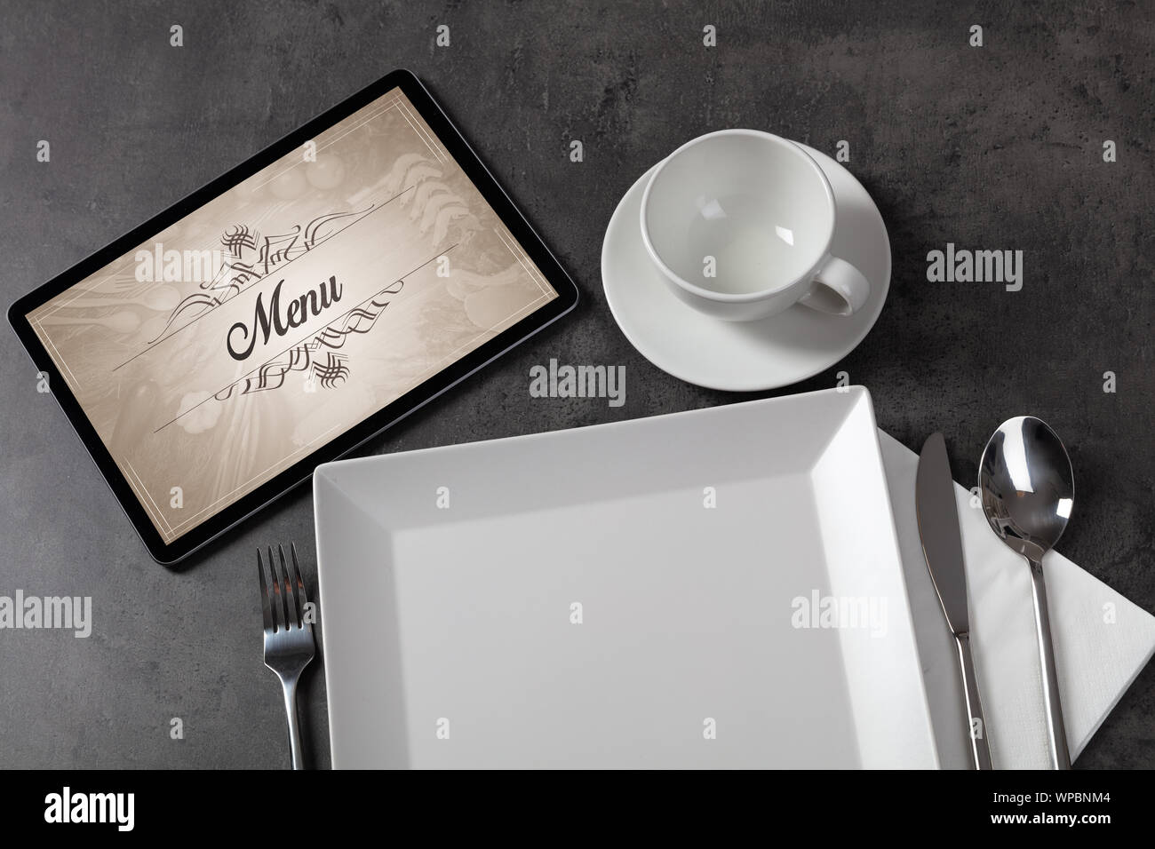 Tablet with stylish restaurant logo and laid table Stock Photo