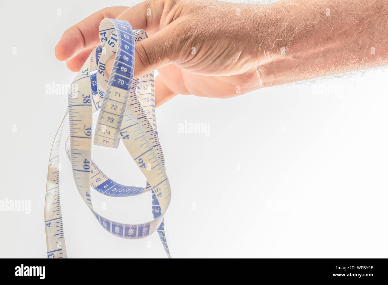 Plastic tape measure held by a hand delicately on a white background. Space to write. Stock Photo