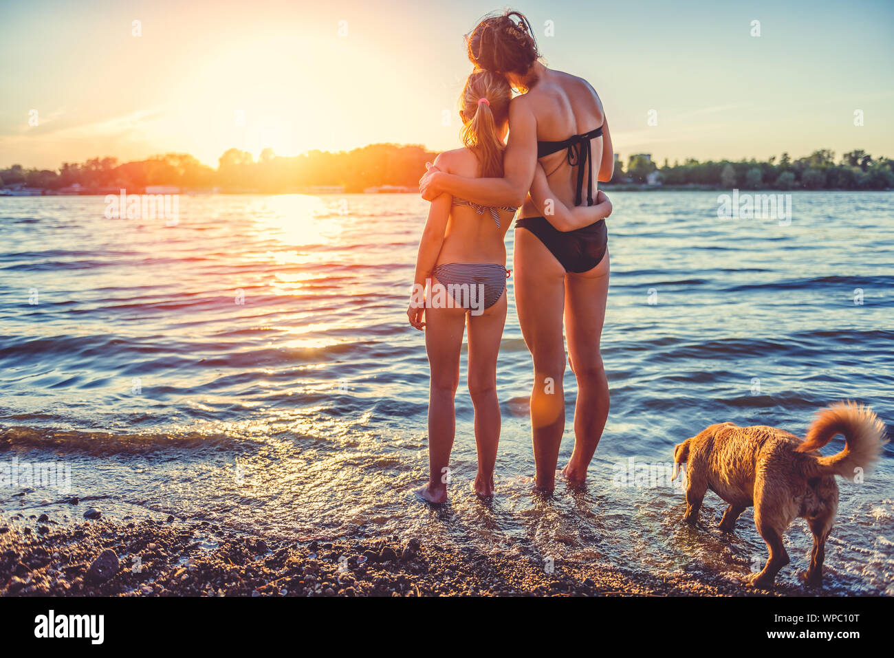 Mother, daughter and small yellow dog enjoying on the beach Stock Photo