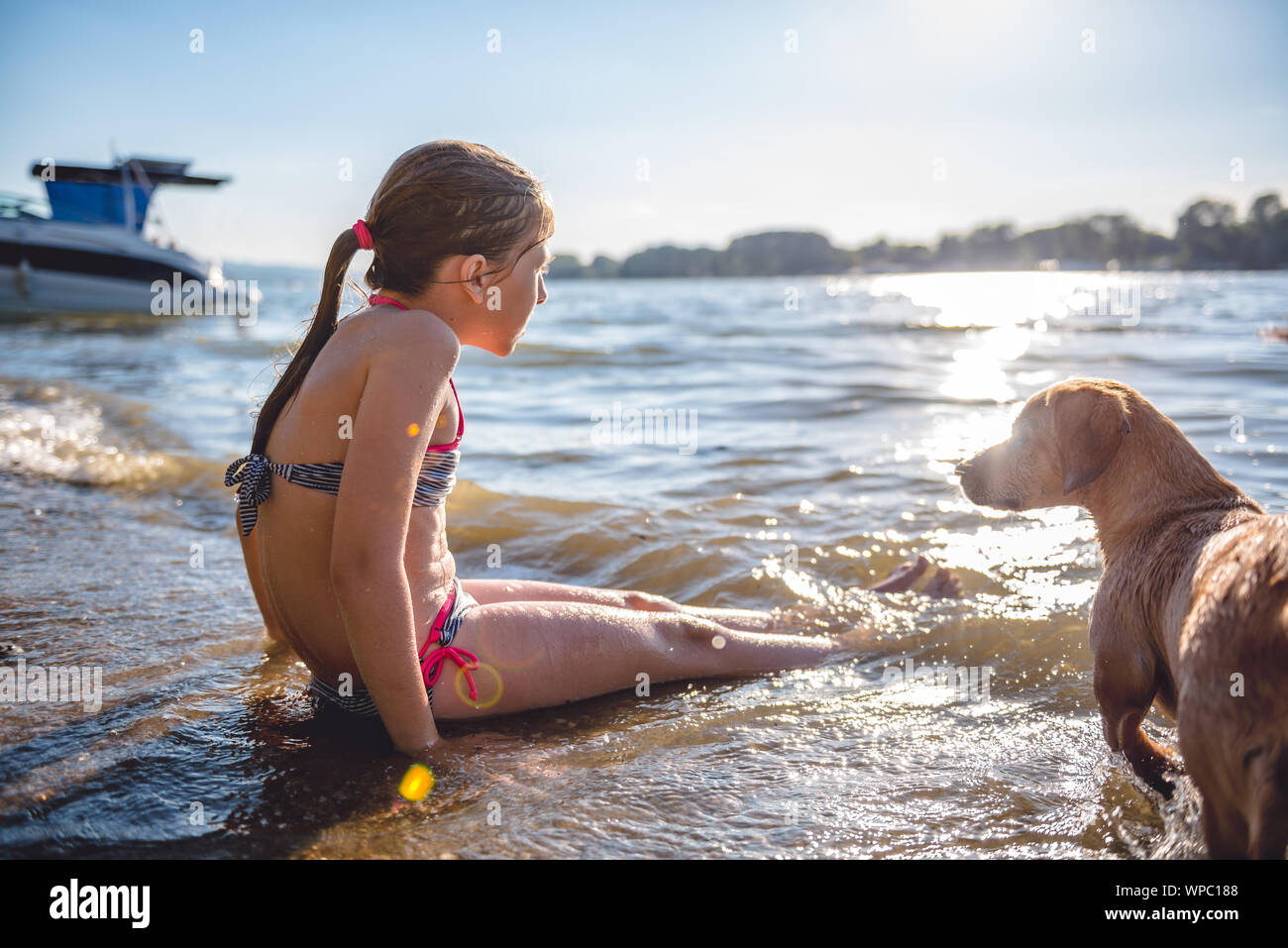 Girl sitting on the beach with a small yellow dog Stock Photo